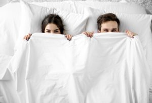 unhappy couple peering out from under marriage sheets