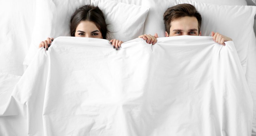 unhappy couple peering out from under marriage sheets