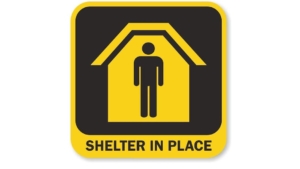 A sign showing a figure inside a house, with the caption "Shelter in Place."